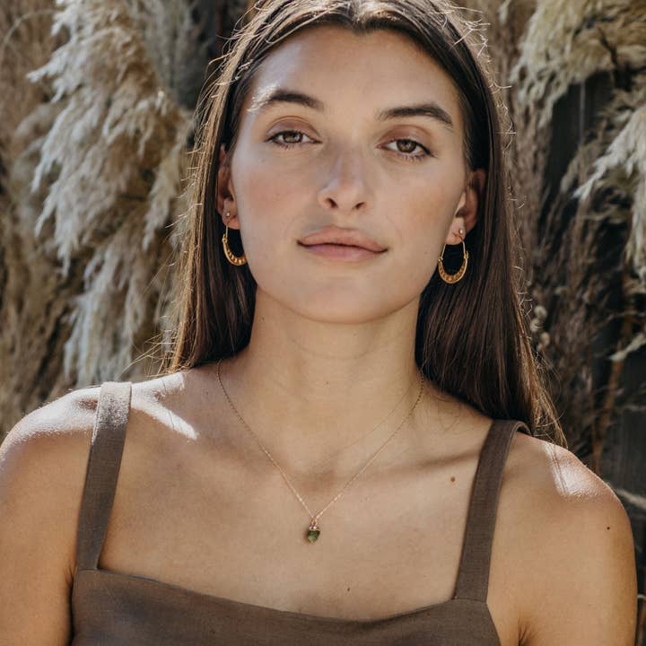 Woman wearing gold hoop earrings and a necklace against a natural background