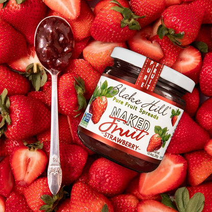 A jar of Blake Hill Strawberry preserves on a bed of strawberries with a spoonful of preserves.
