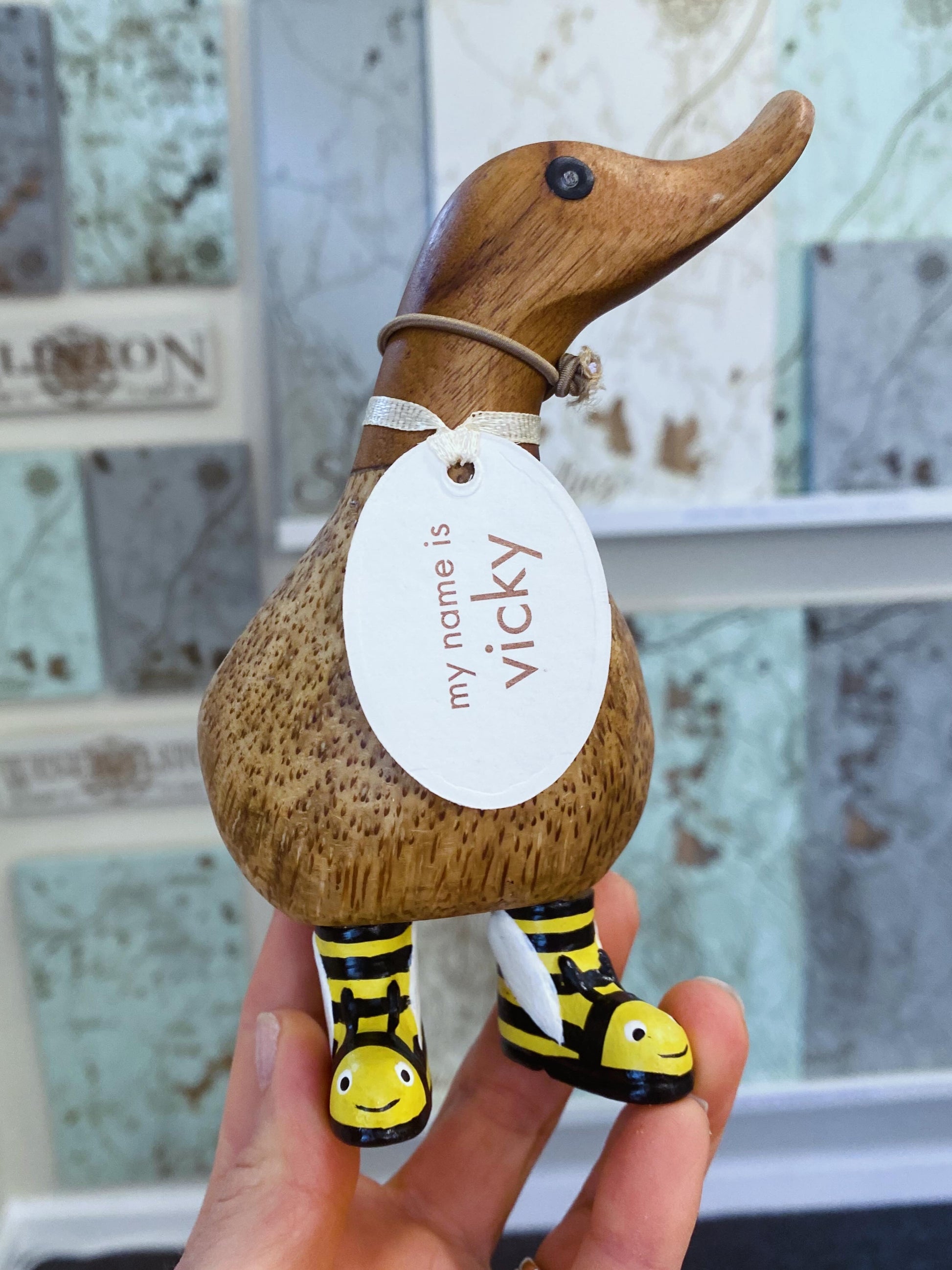 Wooden duck figurine with a 'my name is Vicky' tag held by a hand.