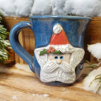 Blue mug with a Santa Claus face design on a wooden surface with snow-like texture.