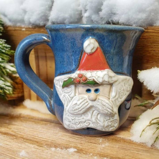 Blue mug with a Santa Claus face design on a wooden surface with snow-like texture.