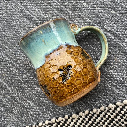 Ceramic mug with textured brown body and turquoise rim on a textured surface