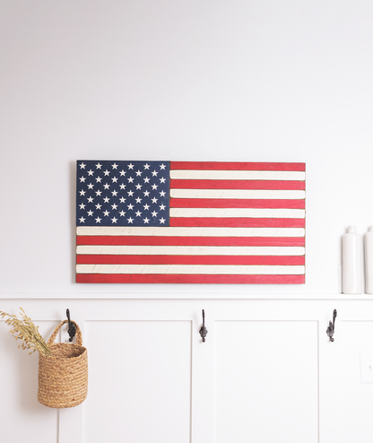 American flag on a white wall above hooks with a basket and candles.