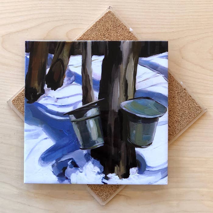 Trivet with tapped maple trees with buckets design on a wooden surface.