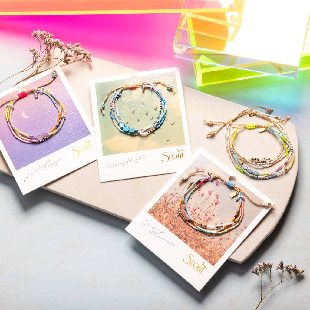 Colorful beaded bracelets on cards with 'Scout' branding, displayed on a gradient background.