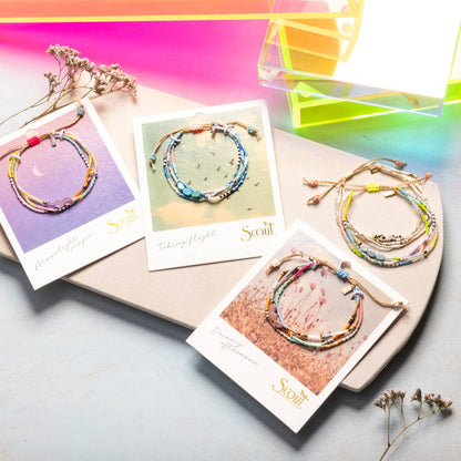 Colorful beaded bracelets on cards with 'Scout' branding, displayed on a gradient background.