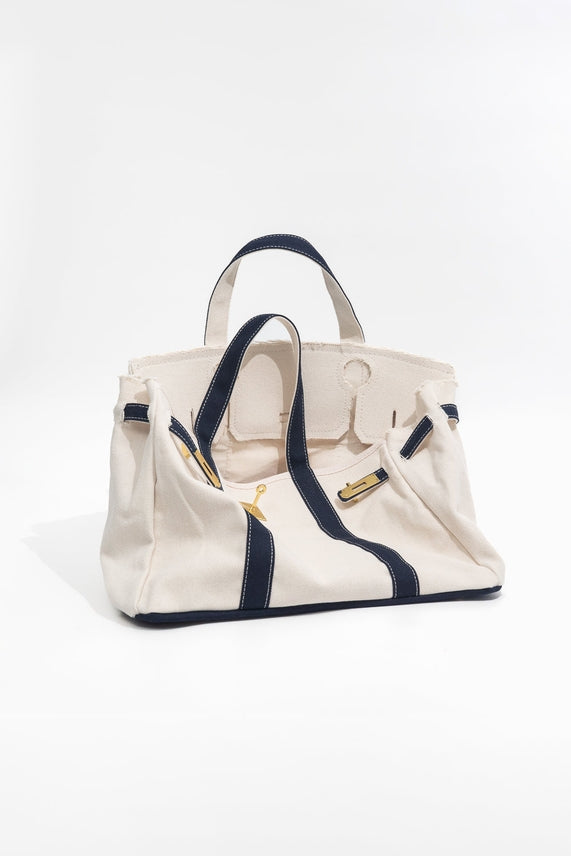 Beige handbag with navy accents folded open to show interior on a white background
