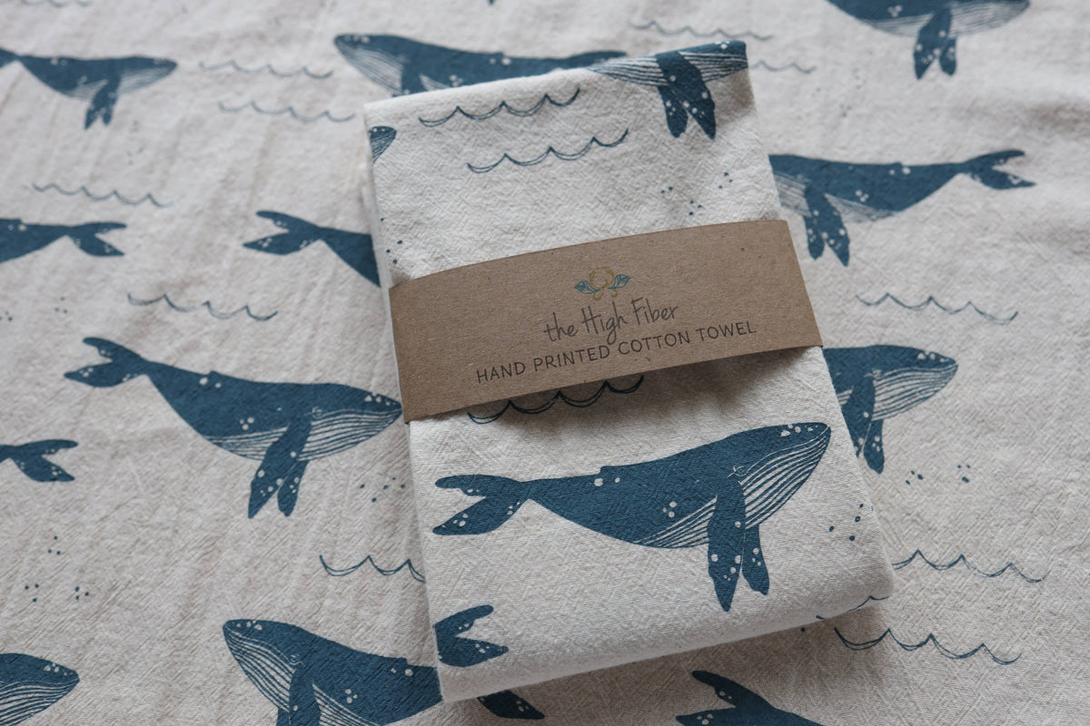 Folded towel with whale design and 'The High Fiber' label on a matching patterned background