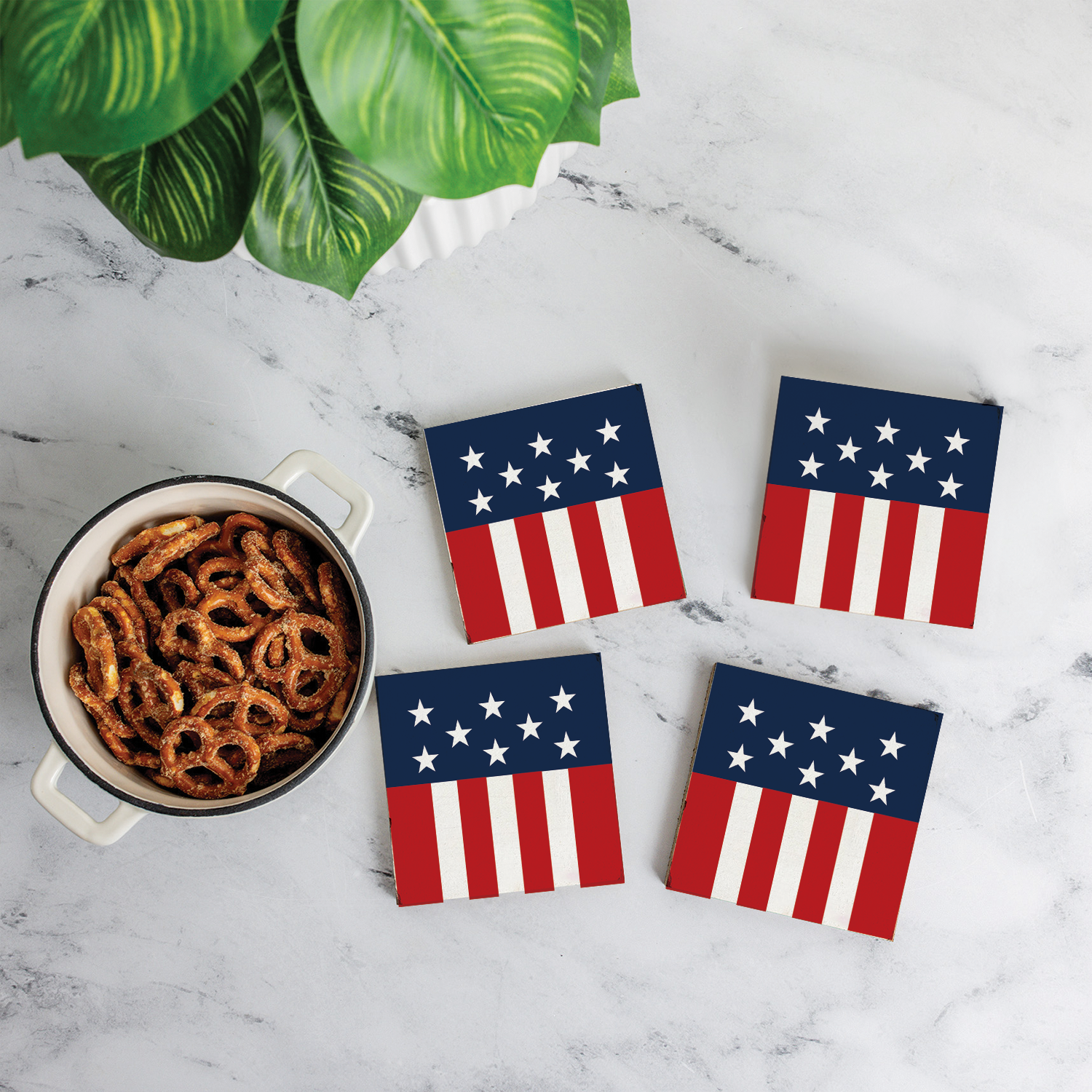 Four American flag coasters on a marble surface with a bowl of pretzels.