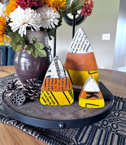 Decorative candy corn shaped objects on a wooden tray with flowers in the background