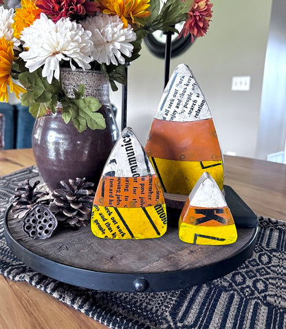 Decorative candy corn shaped objects on a wooden tray with flowers in the background