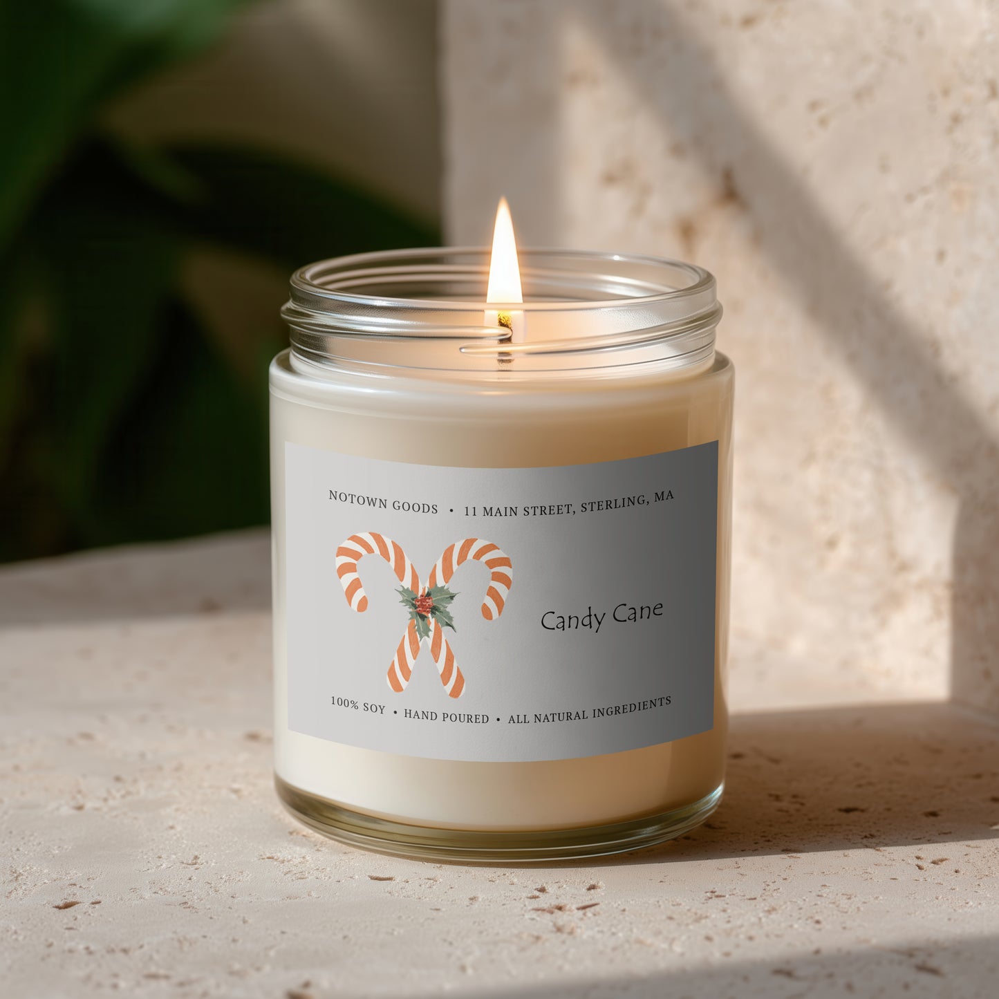 Clear jar candle with white wax and a decorative label on a blurred outdoor background.