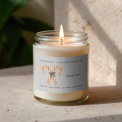 Clear jar candle with white wax and a decorative label on a blurred outdoor background.