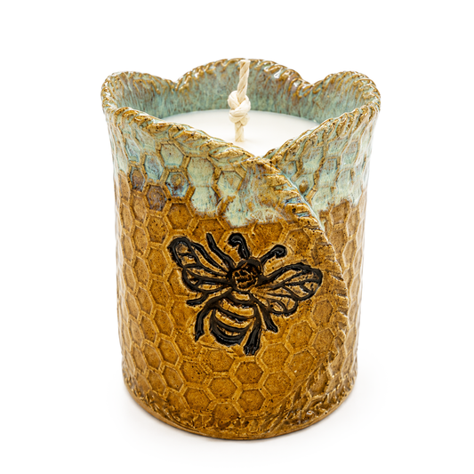 Ceramic candle holder with honeycomb design and bee emblem on a white background