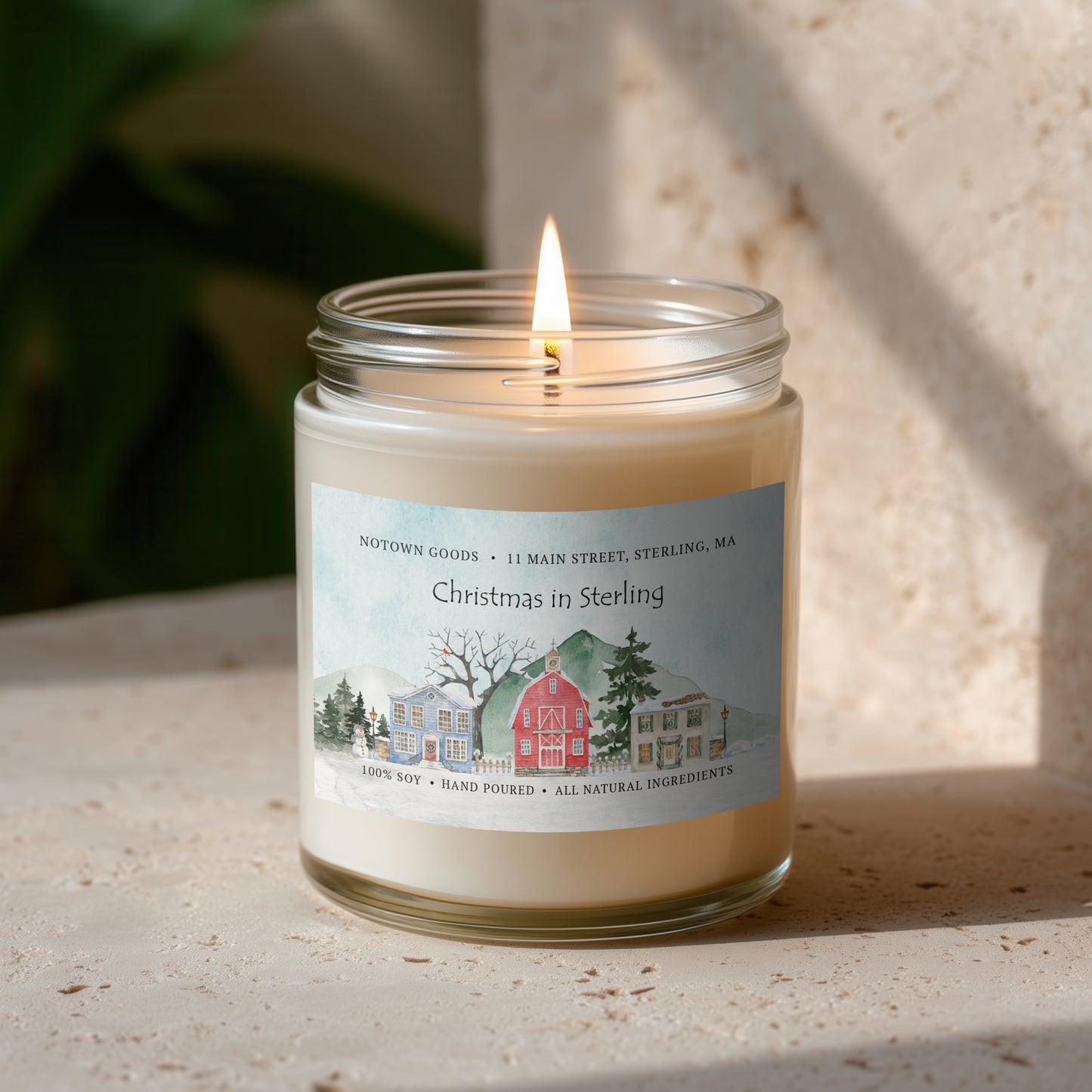 Clear jar candle with white wax and a decorative label on a blurred outdoor background.