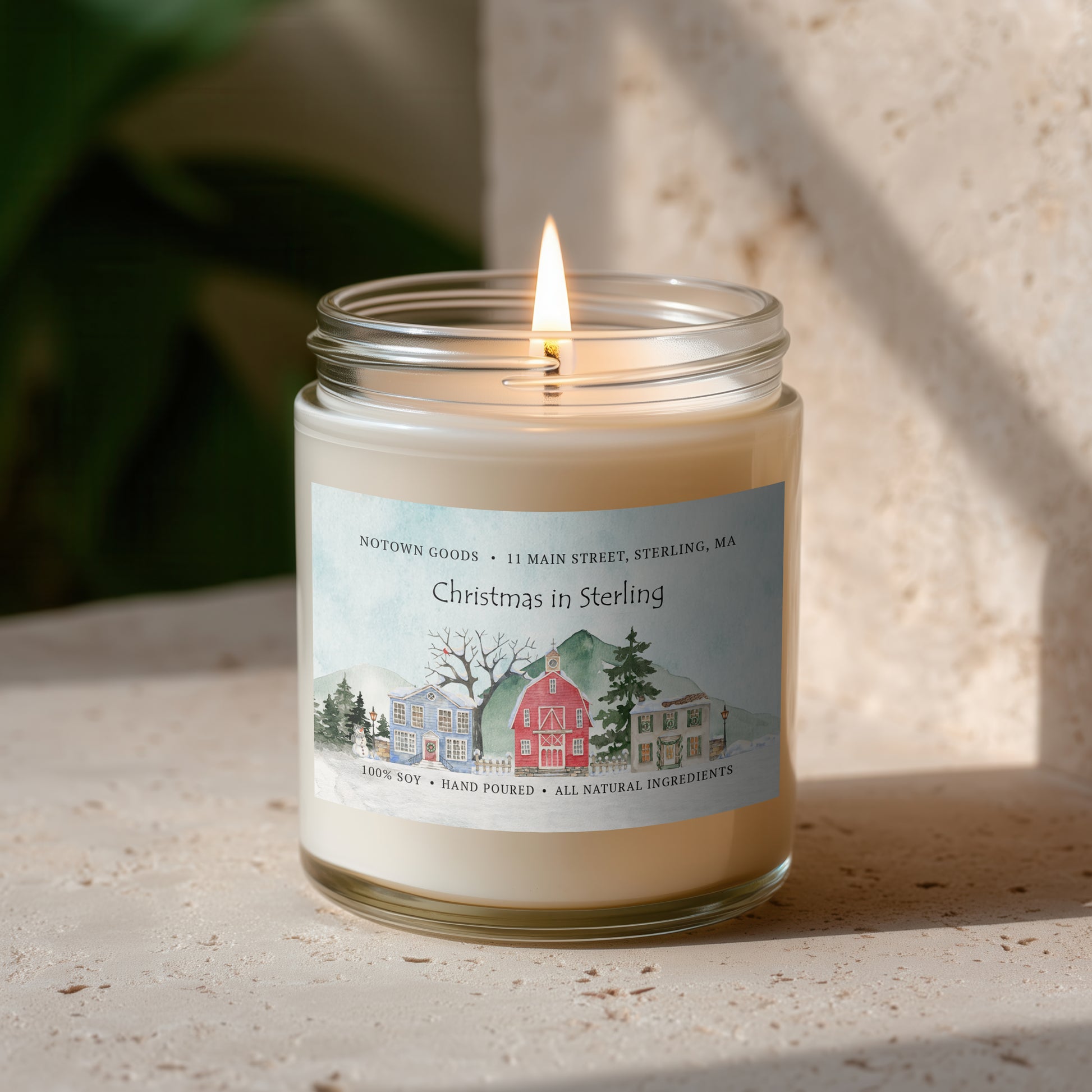 Clear jar candle with white wax and a decorative label on a blurred outdoor background.