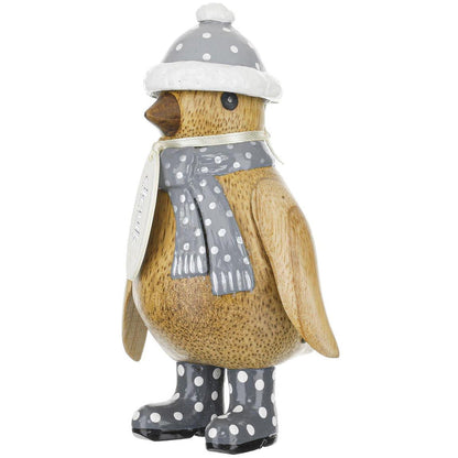 Wooden penguin figurine wearing a gray hat, scarf, and boots with white polka dots on a white background.