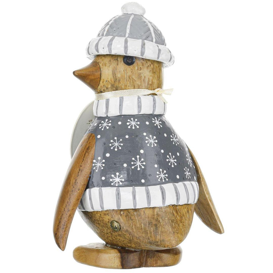 Wooden penguin figurine wearing a gray sweater with snowflake pattern and a striped hat on a white background.
