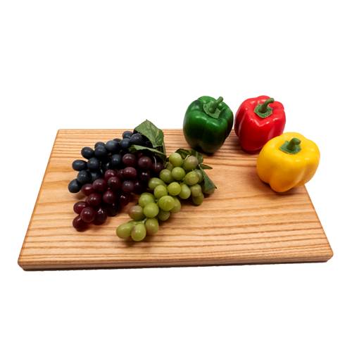 Wooden cutting board with grapes, green pepper, red pepper, and yellow pepper on a white background