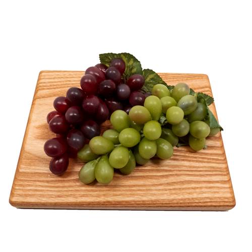 Bunches of red and green grapes on a wooden cutting board with a white background