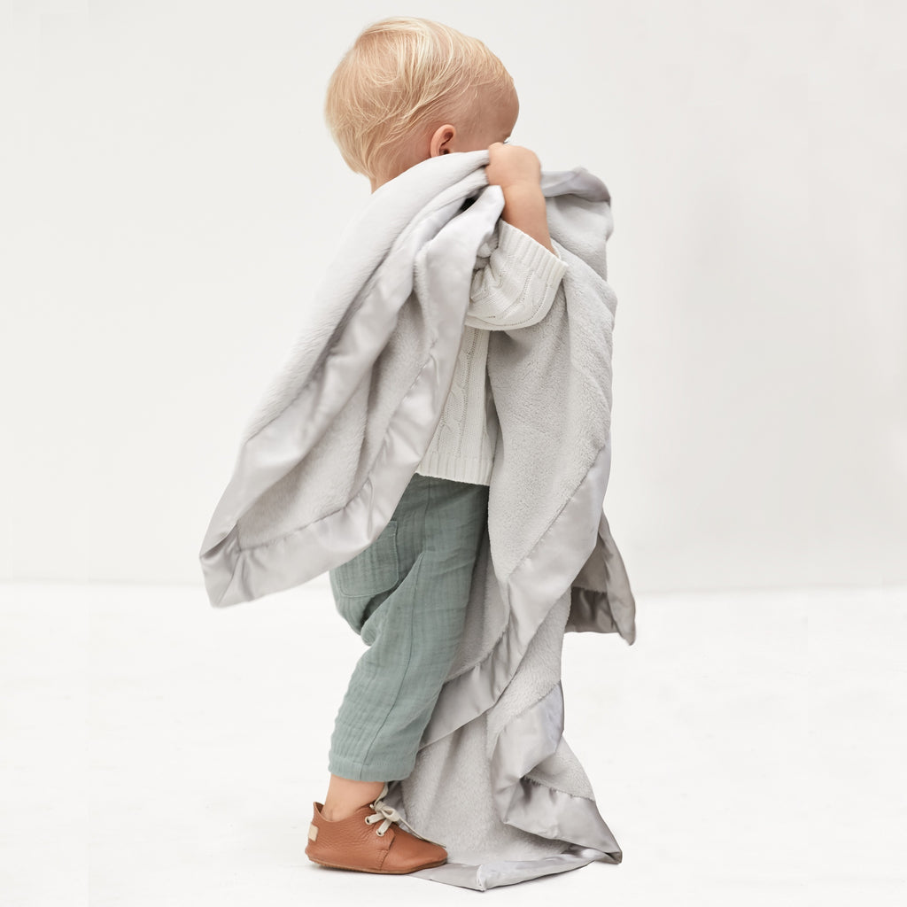 Child holding a light gray blanket against a white background