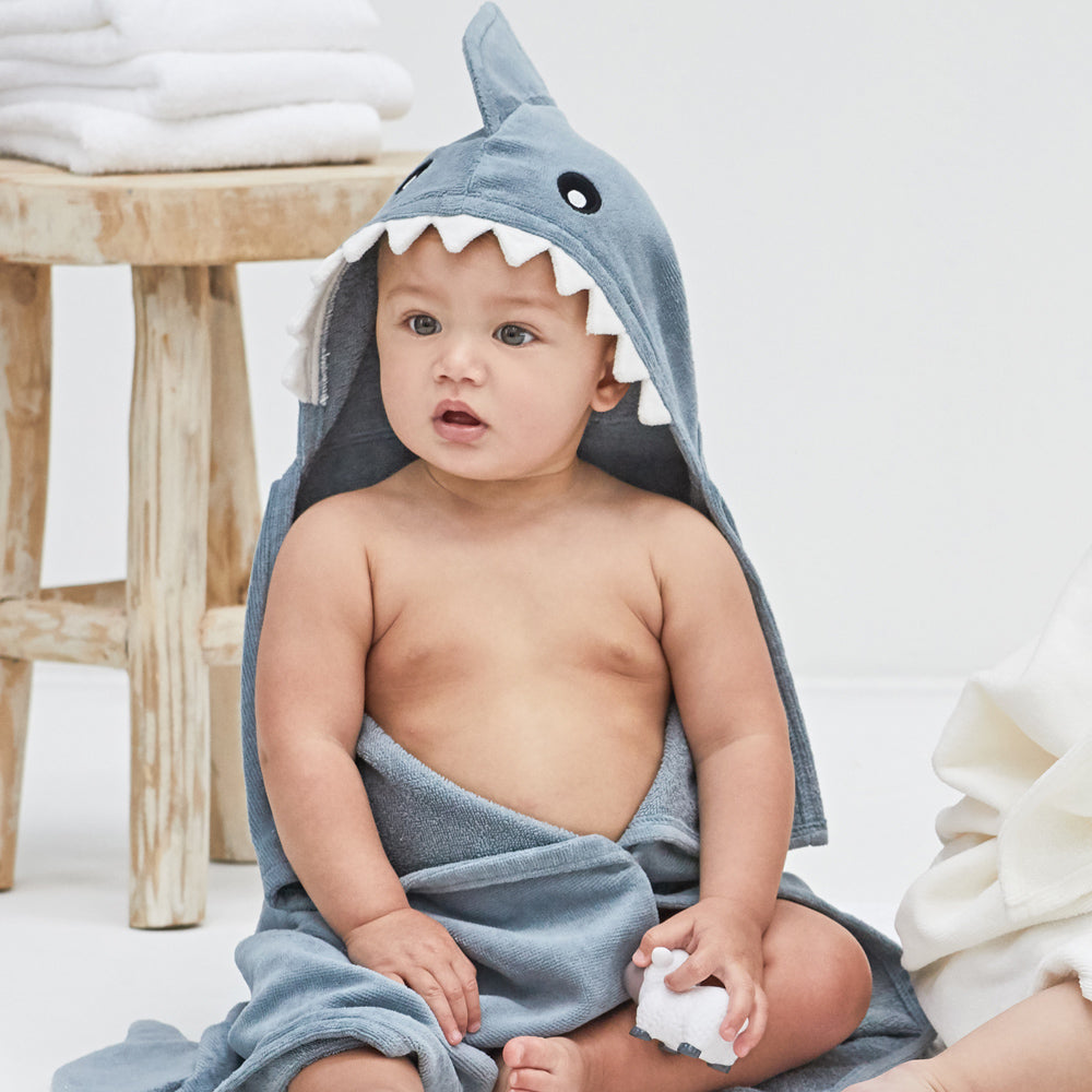 Baby wearing a shark-shaped hooded towel sitting on a white surface.