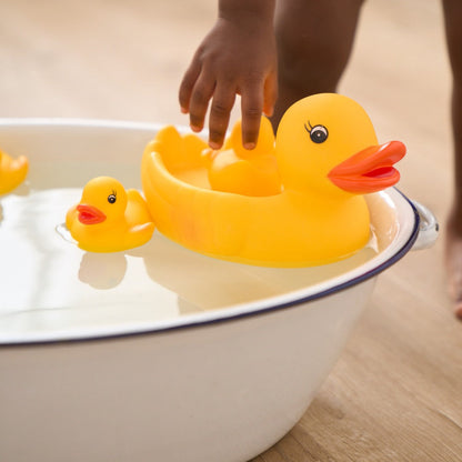 Yellow rubber duck being held over a bathtub with another duck inside.