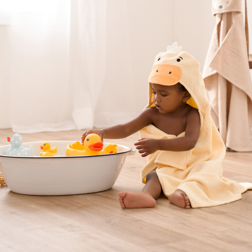 Child in a yellow duck towel playing with rubber ducks in a small bathtub.