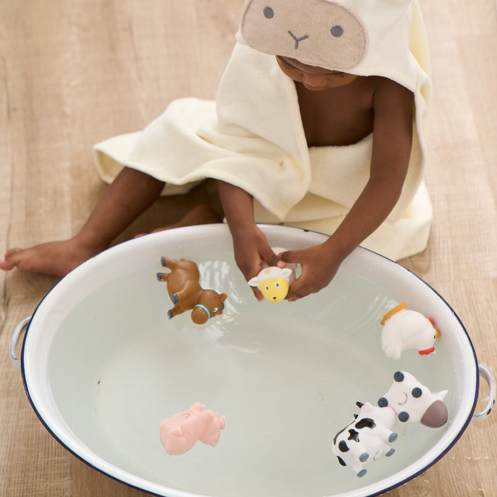 Child playing with animal toys in a bathtub, wrapped in a towel.