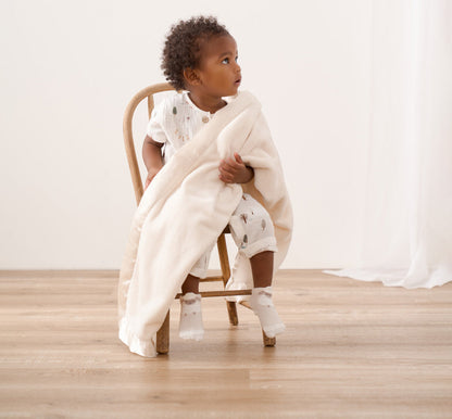 Child sitting on a chair with a cream blanket draped over them in a minimalistic room.