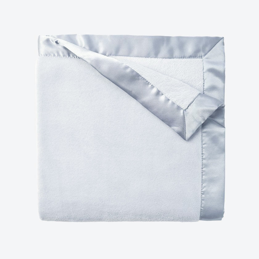 Folded light blue blanket with silver satin trim on a white background