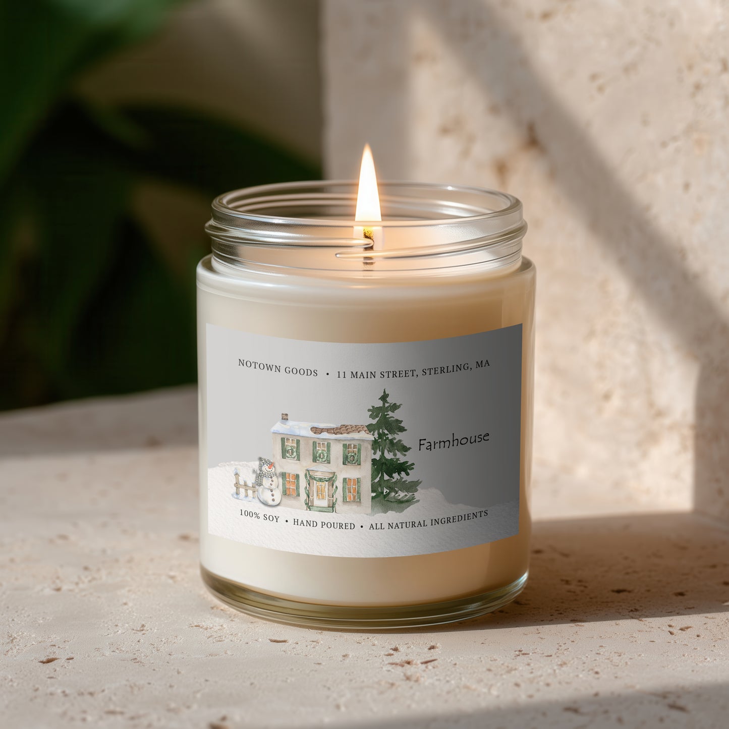 Clear jar candle with white wax and a decorative label on a blurred outdoor background.
