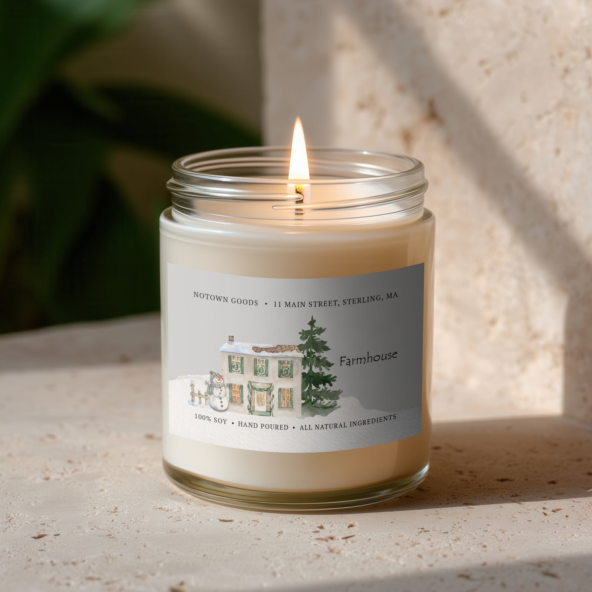 Clear jar candle with white wax and a decorative label on a blurred outdoor background.