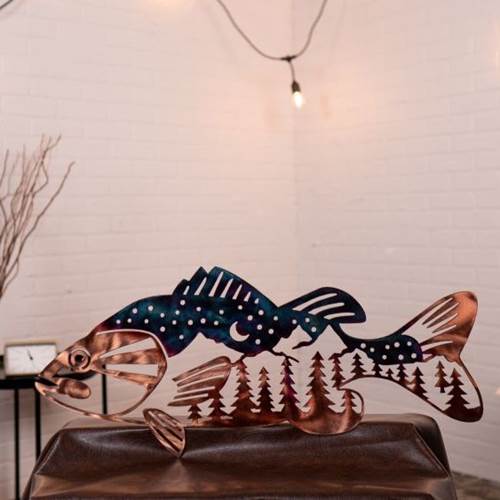 Metal fish sculpture with forest design on a wooden surface