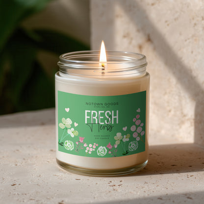 Clear jar candle with white wax and a decorative label on a blurred outdoor background.