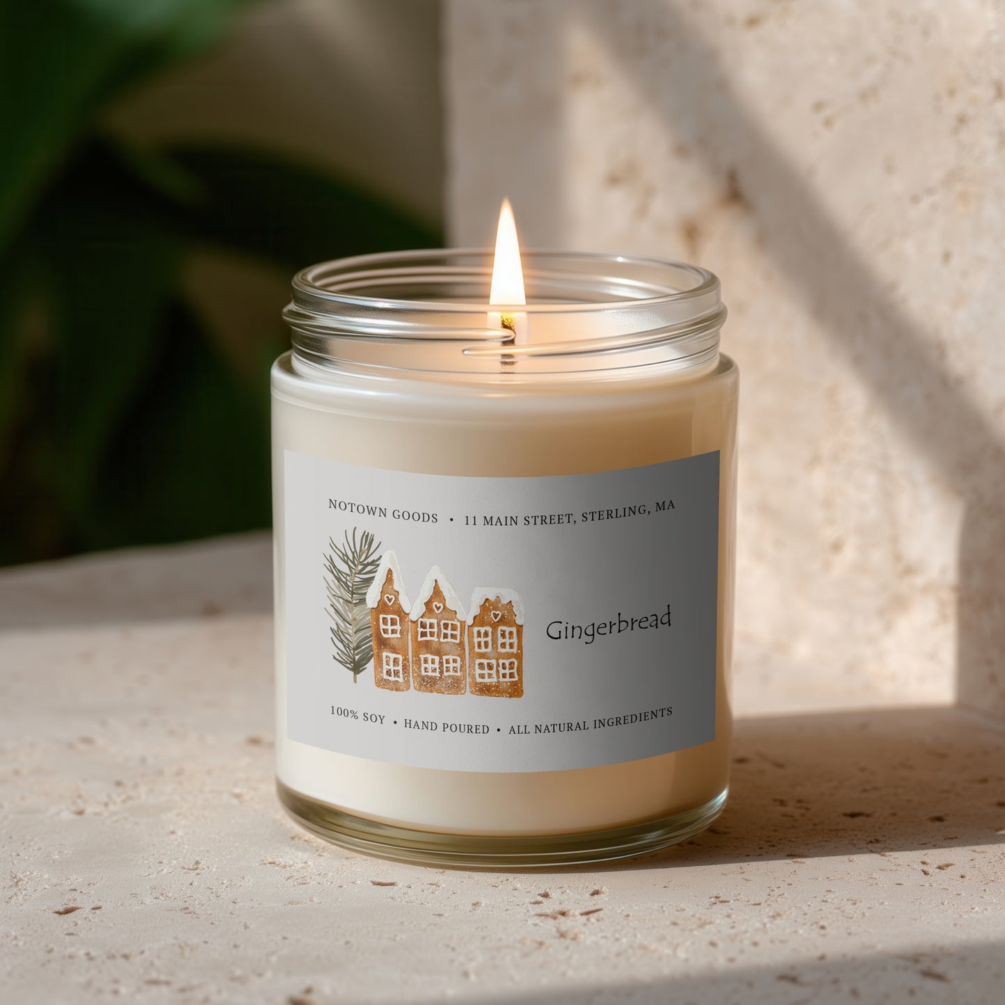 Clear jar candle with white wax and a decorative label on a blurred outdoor background.