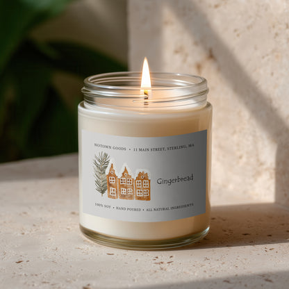 Clear jar candle with white wax and a decorative label on a blurred outdoor background.