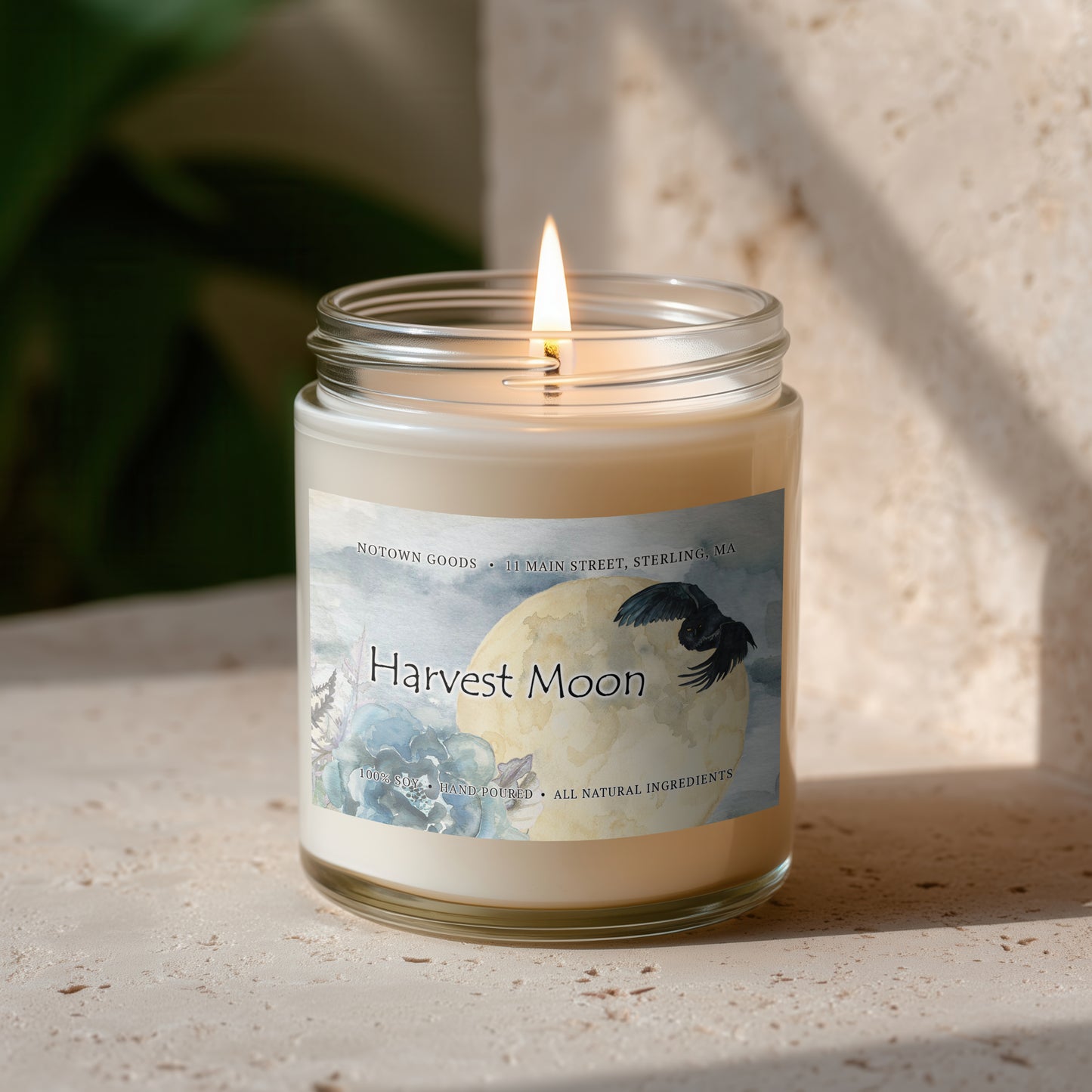 Clear jar candle with white wax and a decorative label on a blurred outdoor background.