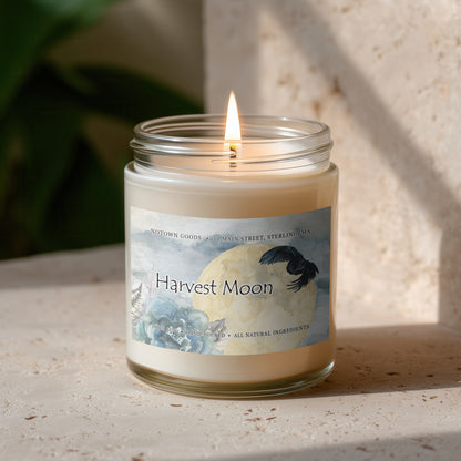 Clear jar candle with white wax and a decorative label on a blurred outdoor background.