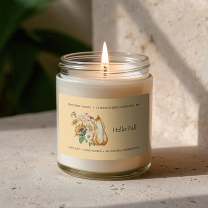 Clear jar candle with white wax and a decorative label on a blurred outdoor background.