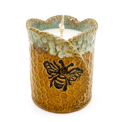 Ceramic candle holder with honeycomb design and bee emblem on a white background