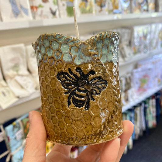Candle with honeycomb and bee design held in front of a store shelf.