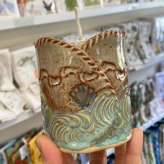 Handmade ceramic candle with wave design held in front of a store shelf.