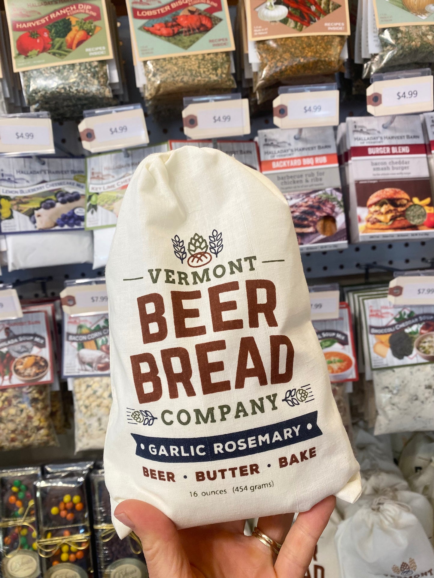 White drawstring bag labeled 'Vermont Beer Bread Company Garlic Rosemary' held in front of a store shelf with various products.