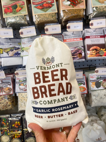 White drawstring bag labeled 'Vermont Beer Bread Company Garlic Rosemary' held in front of a store shelf with various products.
