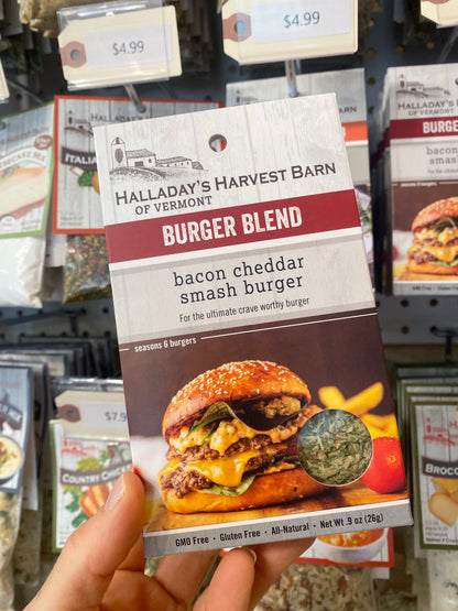 Hand holding a package of Halladay's Harvest Barn Burger Blend in a store setting.