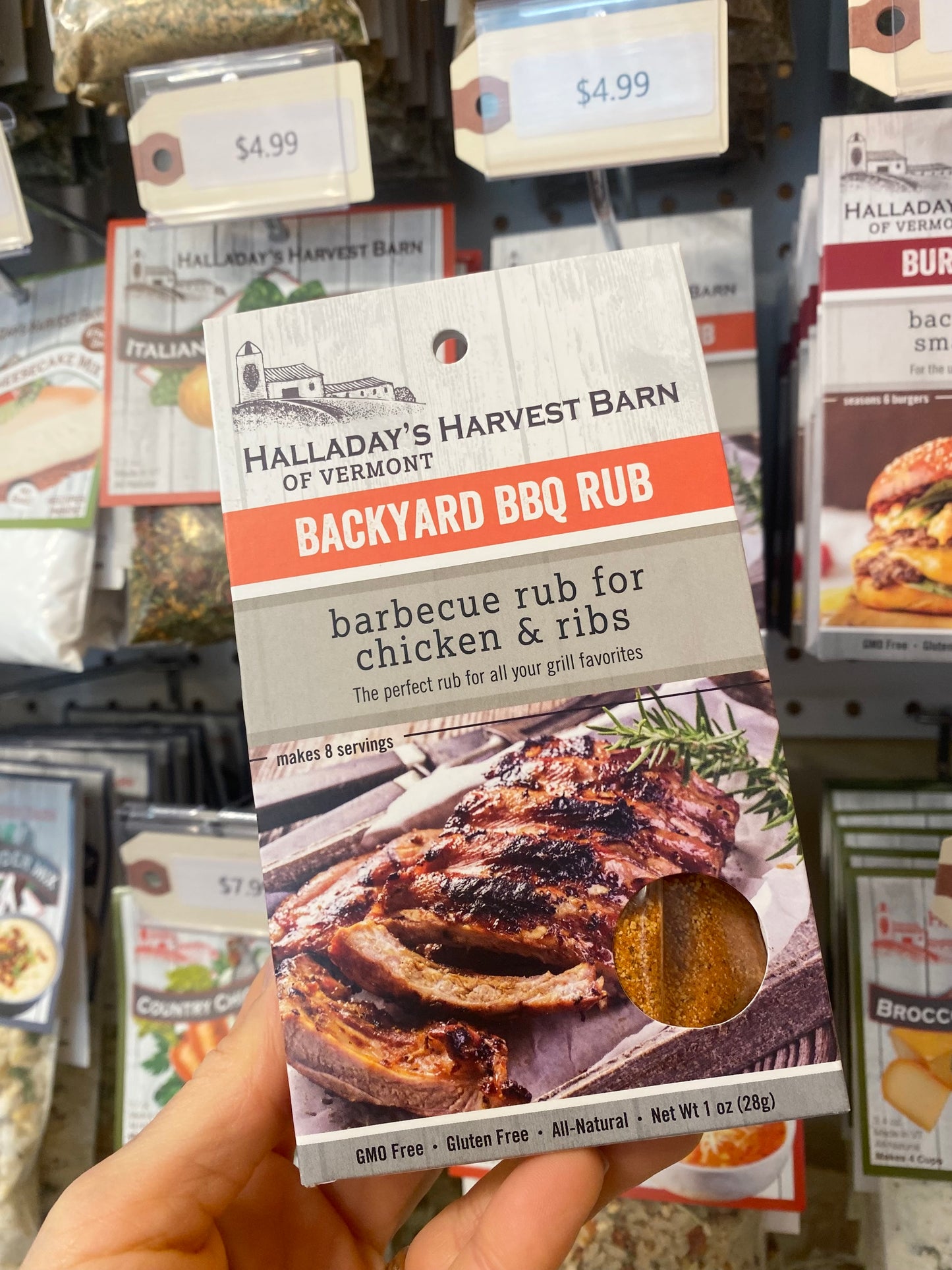 Halladay's Harvest Barn Backyard BBQ Rub package held in front of a store shelf with other products.