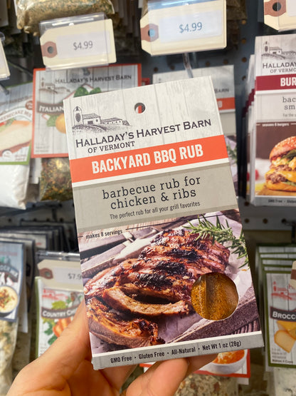 Halladay's Harvest Barn Backyard BBQ Rub package held in front of a store shelf with other products.