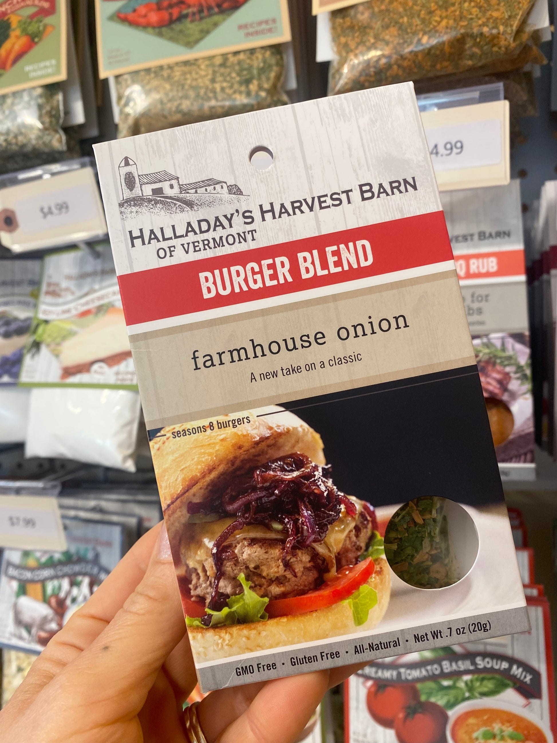 Hand holding a package of Halladay's Harvest Barn Burger Blend farmhouse onion seasoning mix.