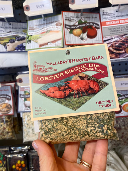Hand holding a package of Halladay's Harvest Barn Lobster Bisque Dip with a store shelf in the background.
